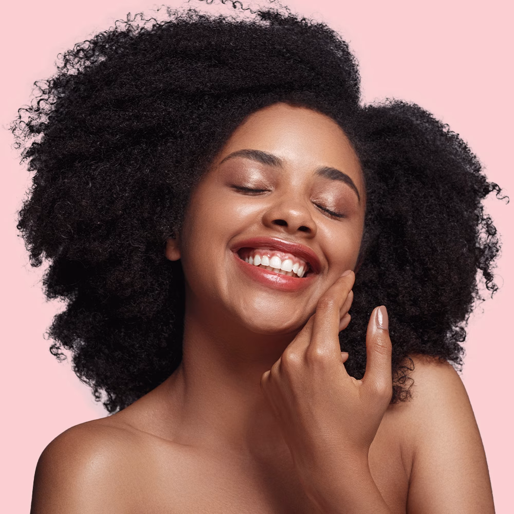 Smiling woman touching face, pink background.