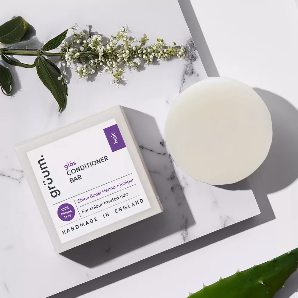 Conditioner bar, box, and green leaves on marble background