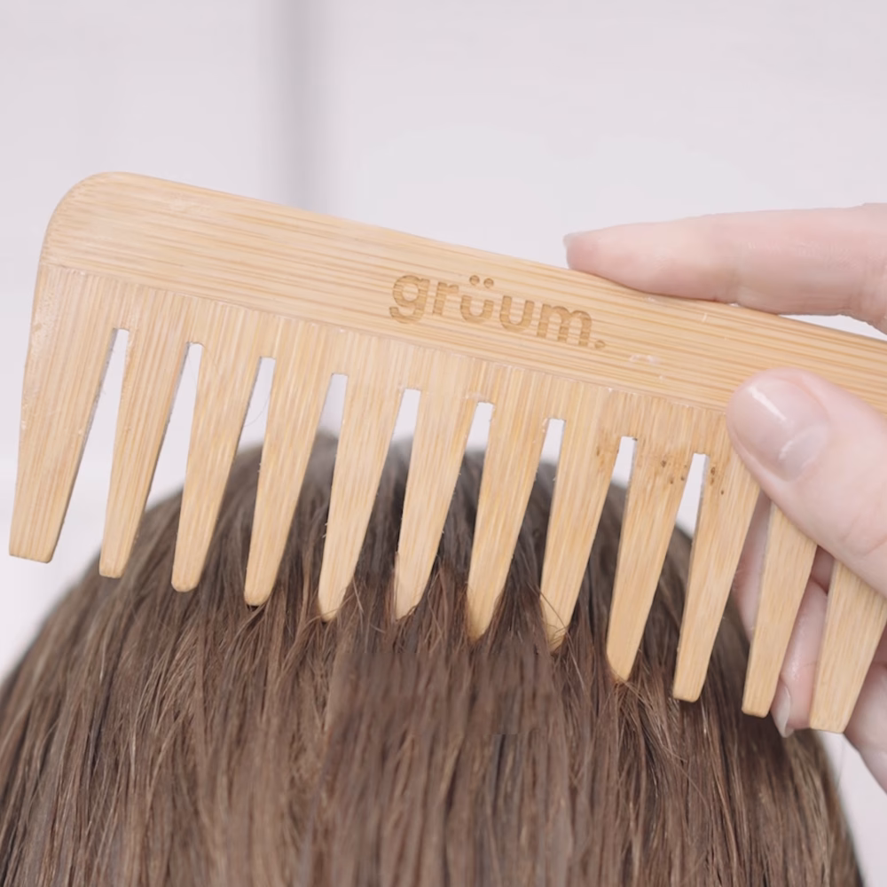 Hand holding wooden comb on hair.