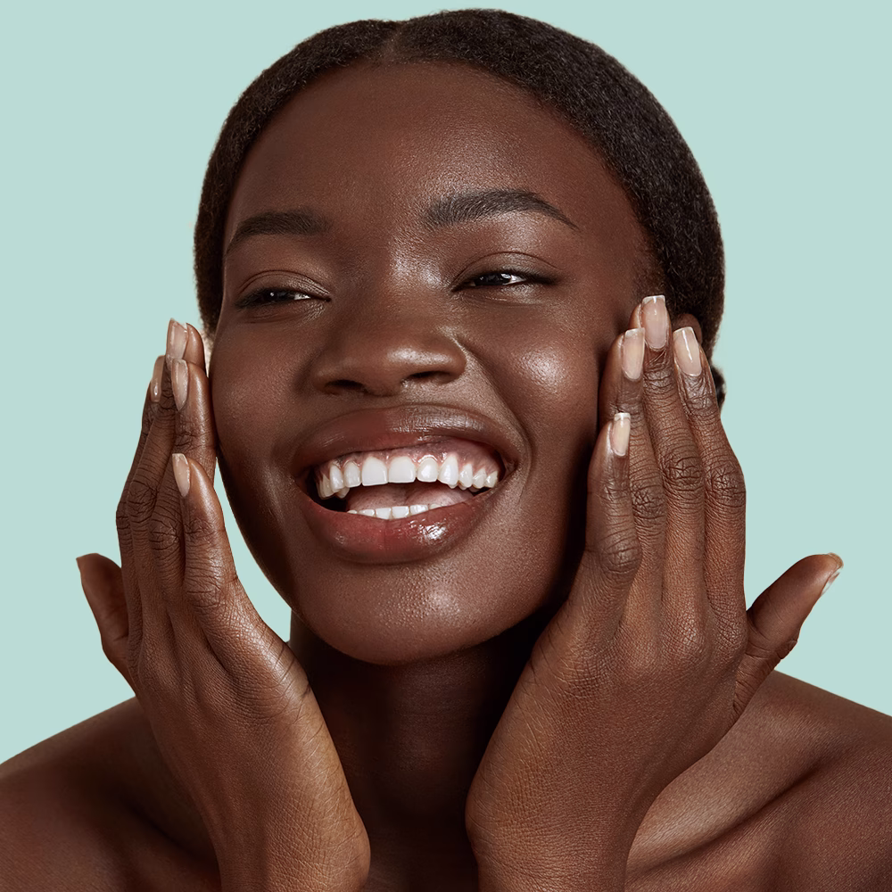 Smiling person touching face against green background.