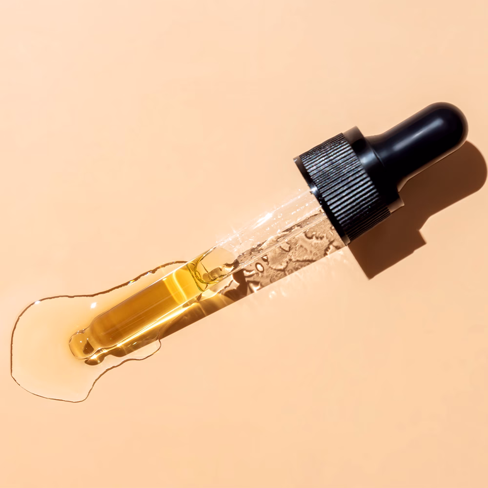 Dropper with oil on peach background.