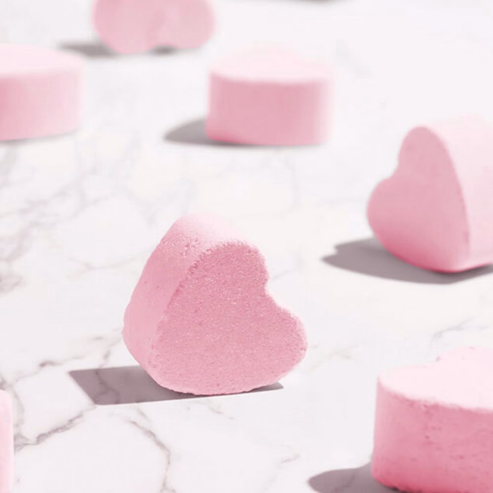 Pink heart-shaped bath bombs on marble surface.