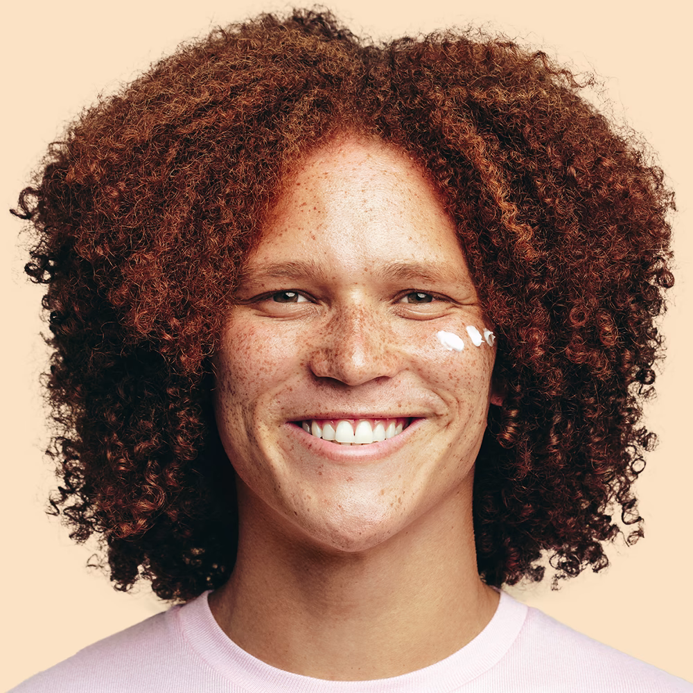 Smiling person with curly hair and freckles.