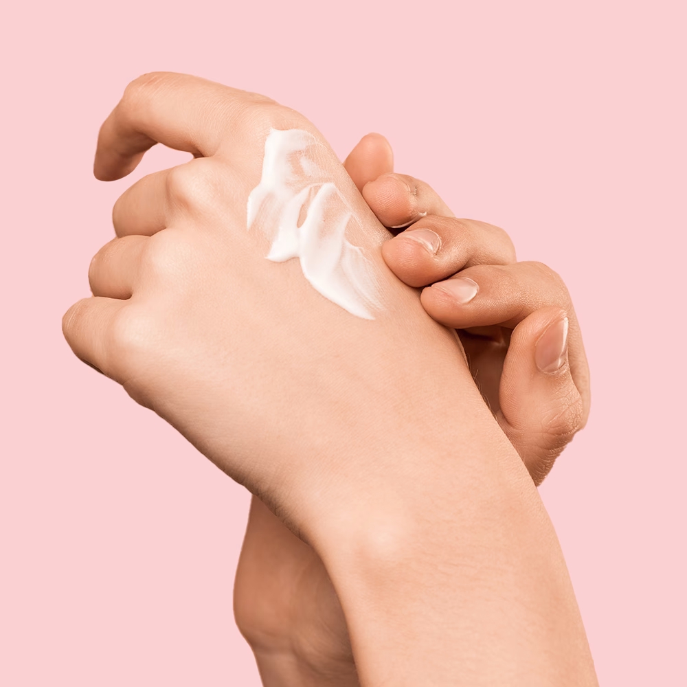 Hands applying cream on skin.