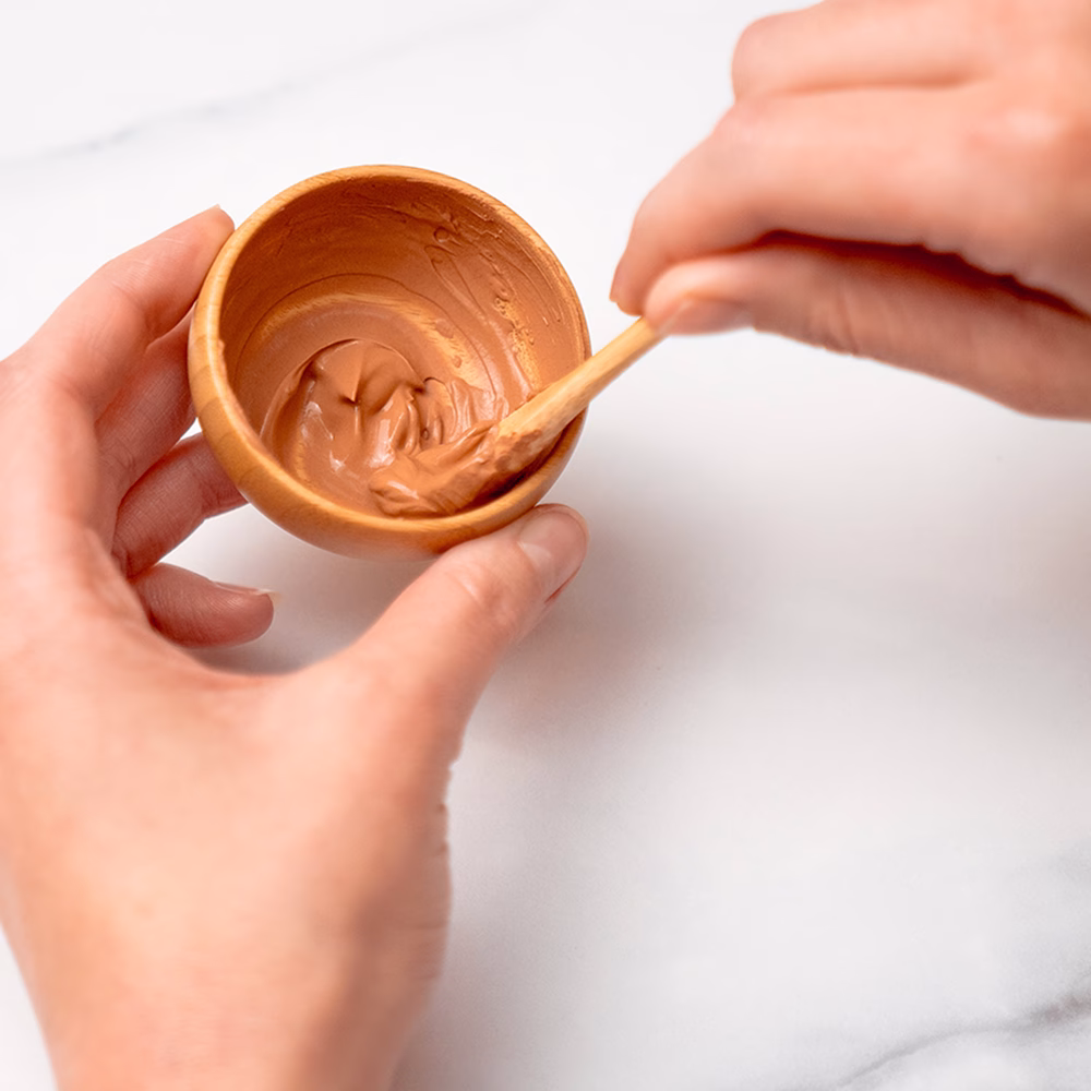 Stirring clay mask in wooden bowl