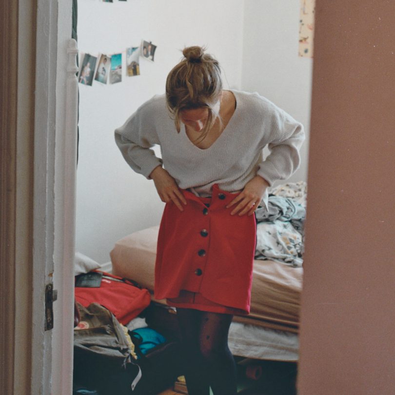 photo of a woman holding a red skirt up to her waist in her bedroom