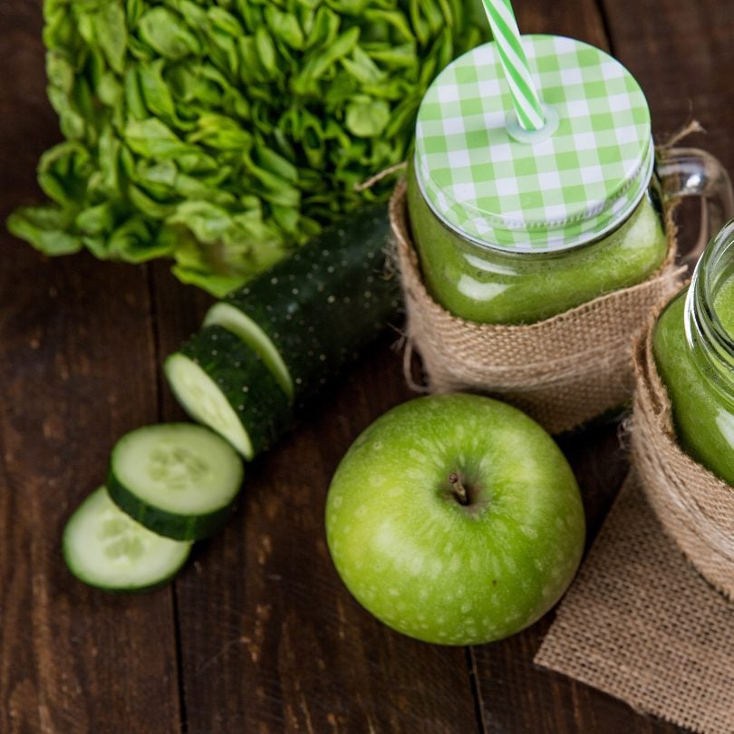 Photo of a sliced cucumber, green apple, green smoothie and green veg